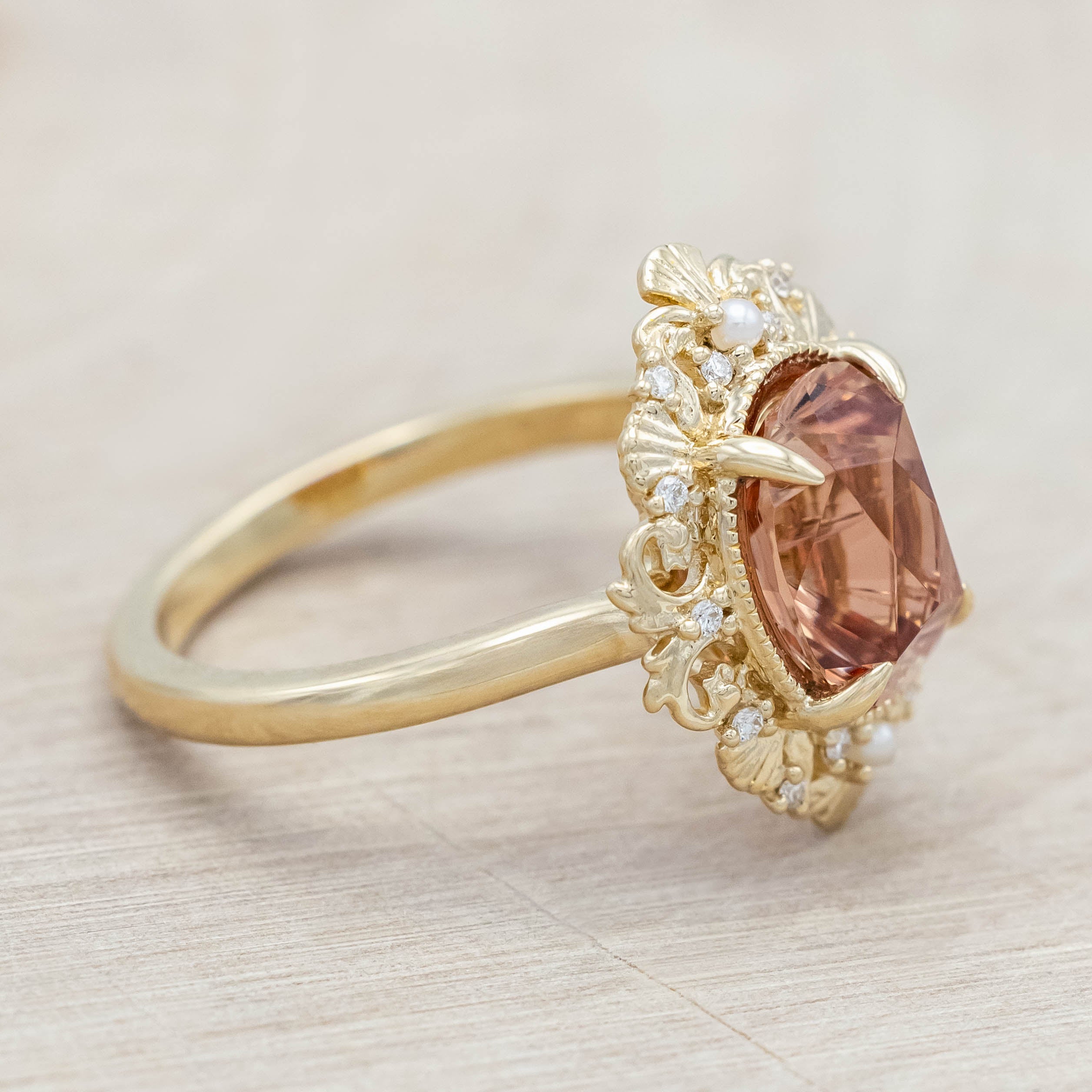 14K yellow gold ring featuring an orange sunstone with small pearls and diamonds on light wooden surface