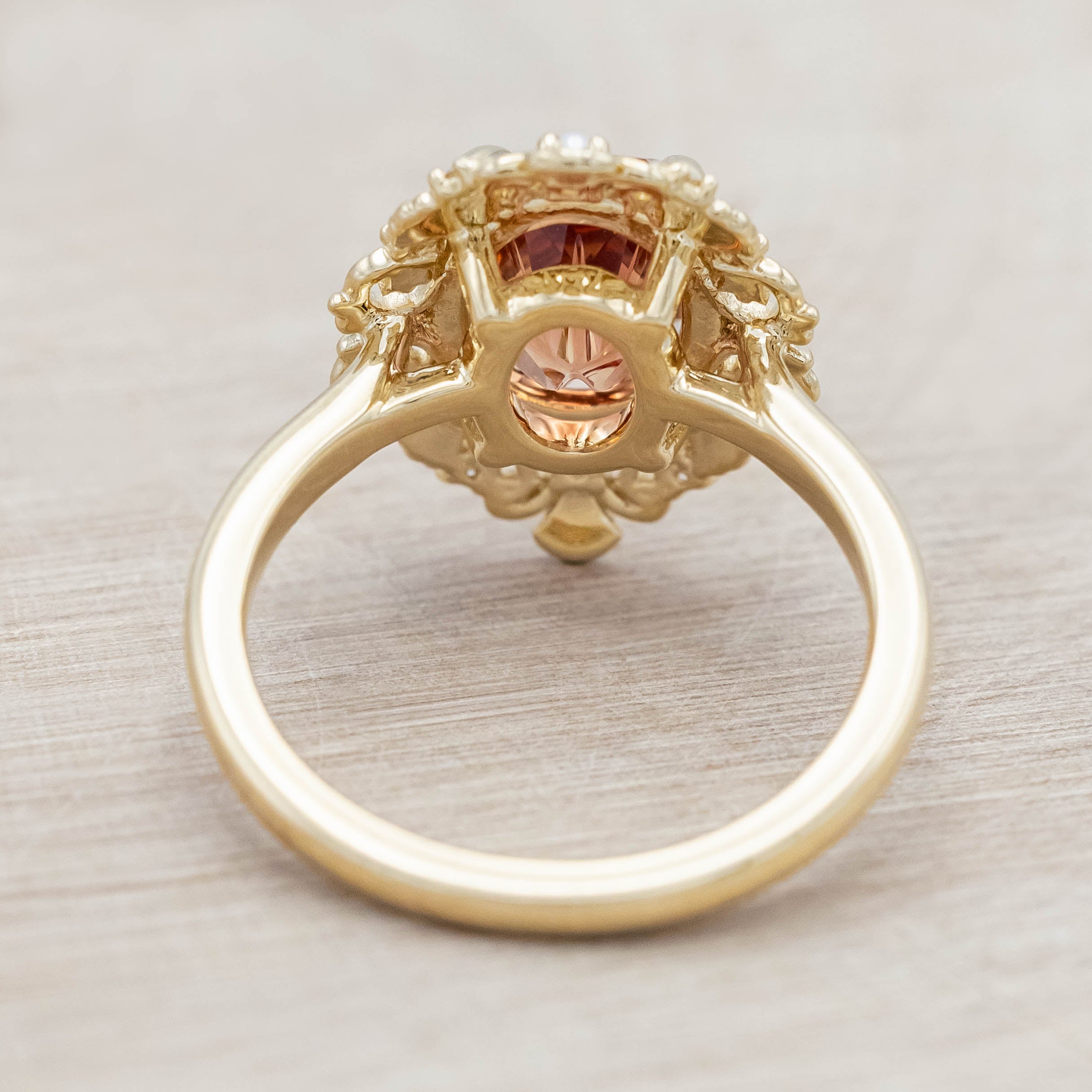 14K yellow gold ring featuring an orange sunstone with small pearls and diamonds on light wooden surface
