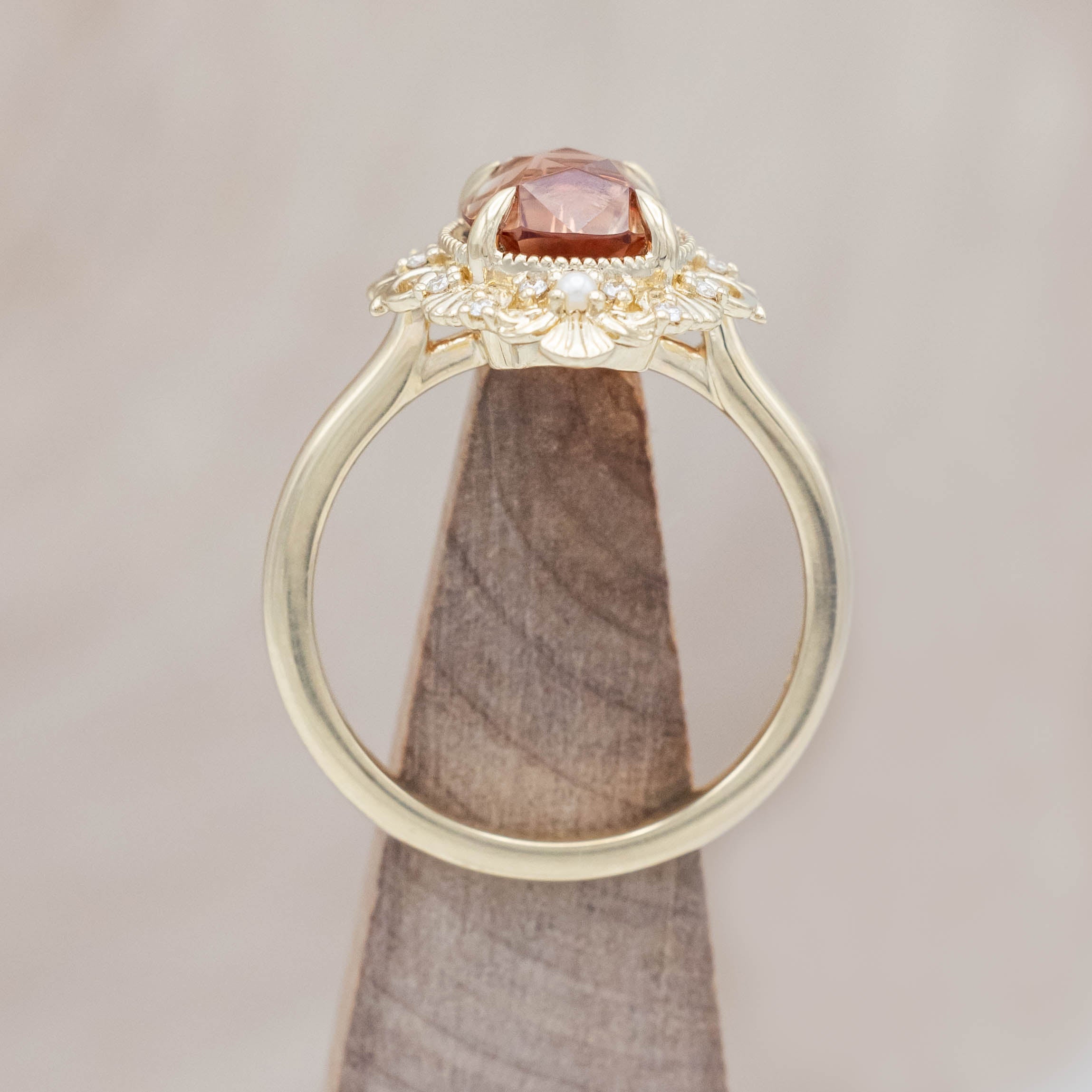 14K yellow gold ring featuring an orange sunstone with small pearls and diamonds on beige background