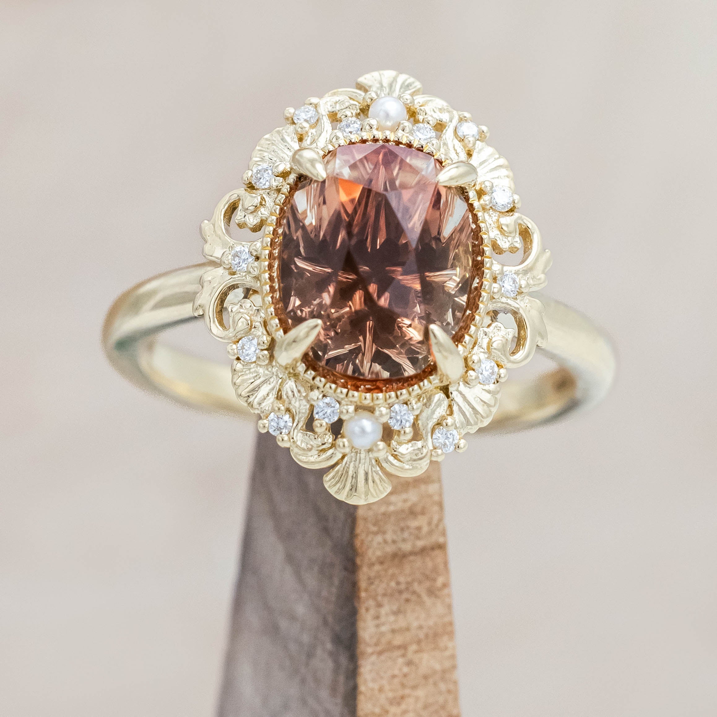 14K yellow gold ring featuring an orange sunstone with small pearls and diamonds on a beige background