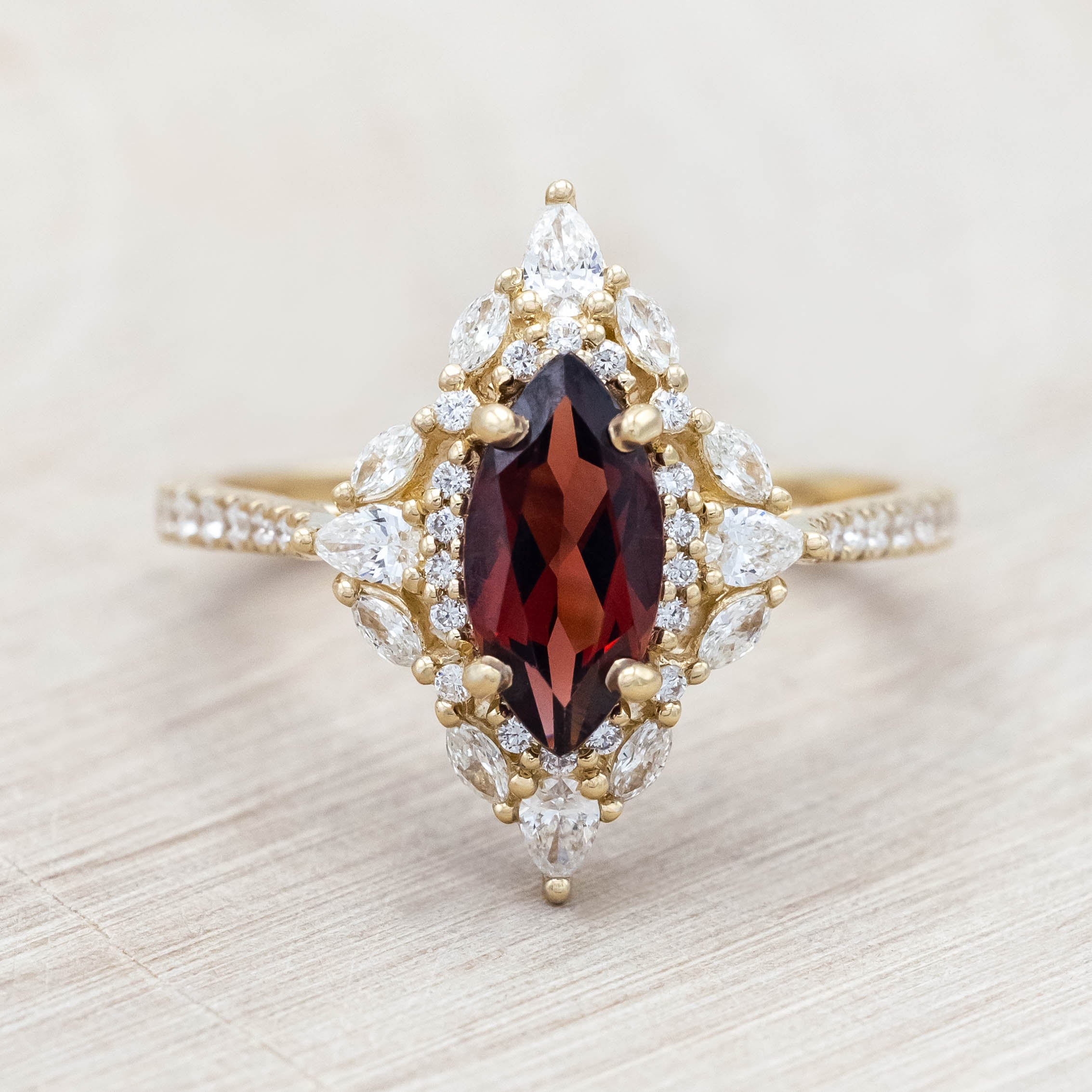 Gold ring with a red garnet and diamond accents on a light wooden background