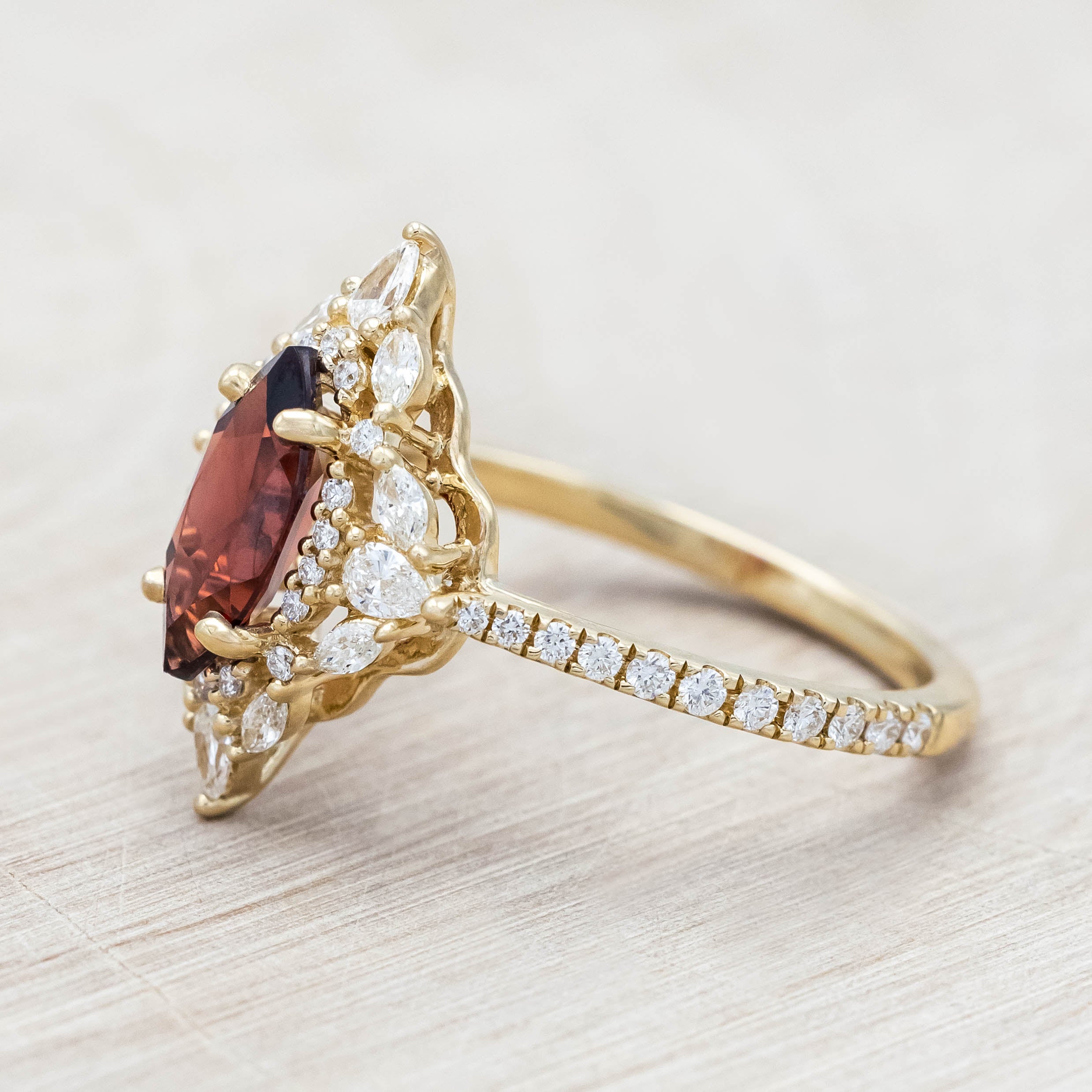 Gold ring with a red garnet and diamond accents on a light wooden background