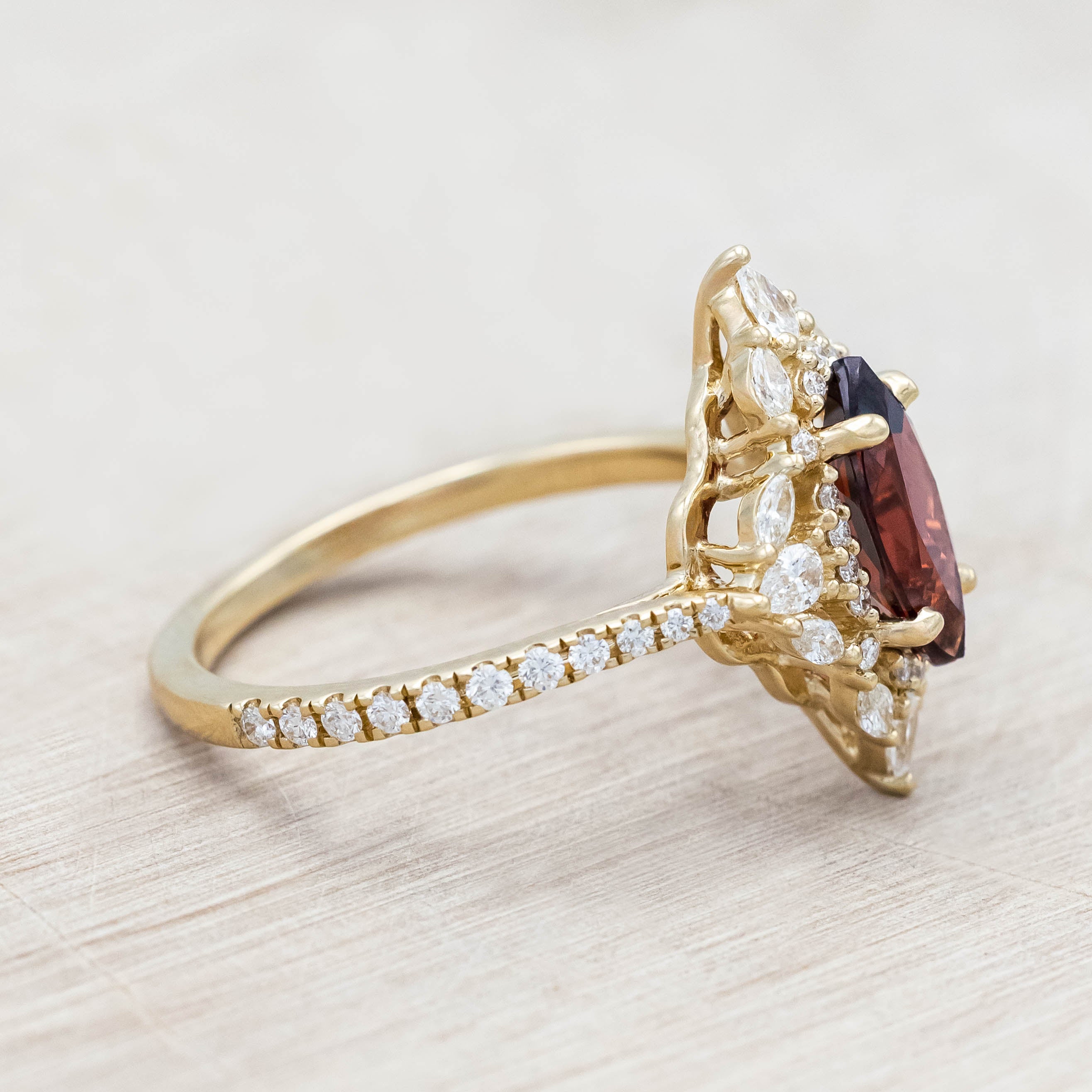 Gold ring with a red garnet and diamond accents on a light wood background