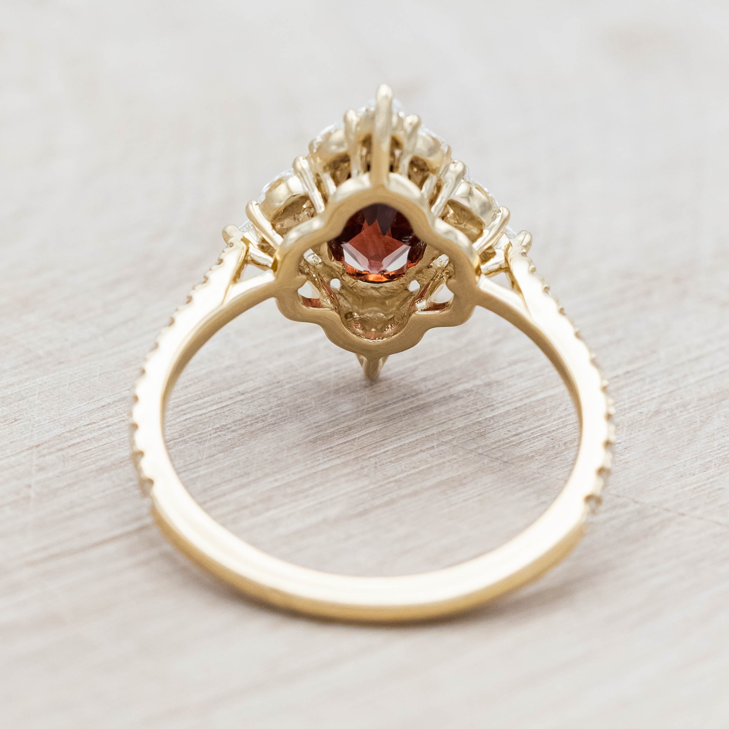 Gold ring with a red garnet and diamond accents on a light wooden background