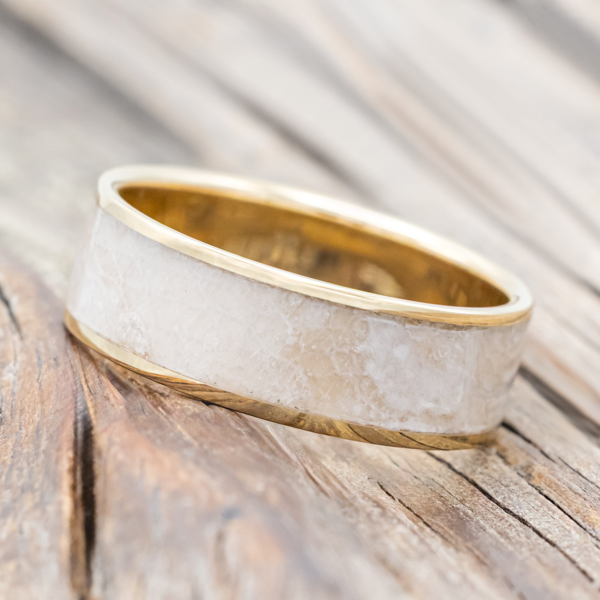 Gold ring with wedding dress inlay on a wooden surface