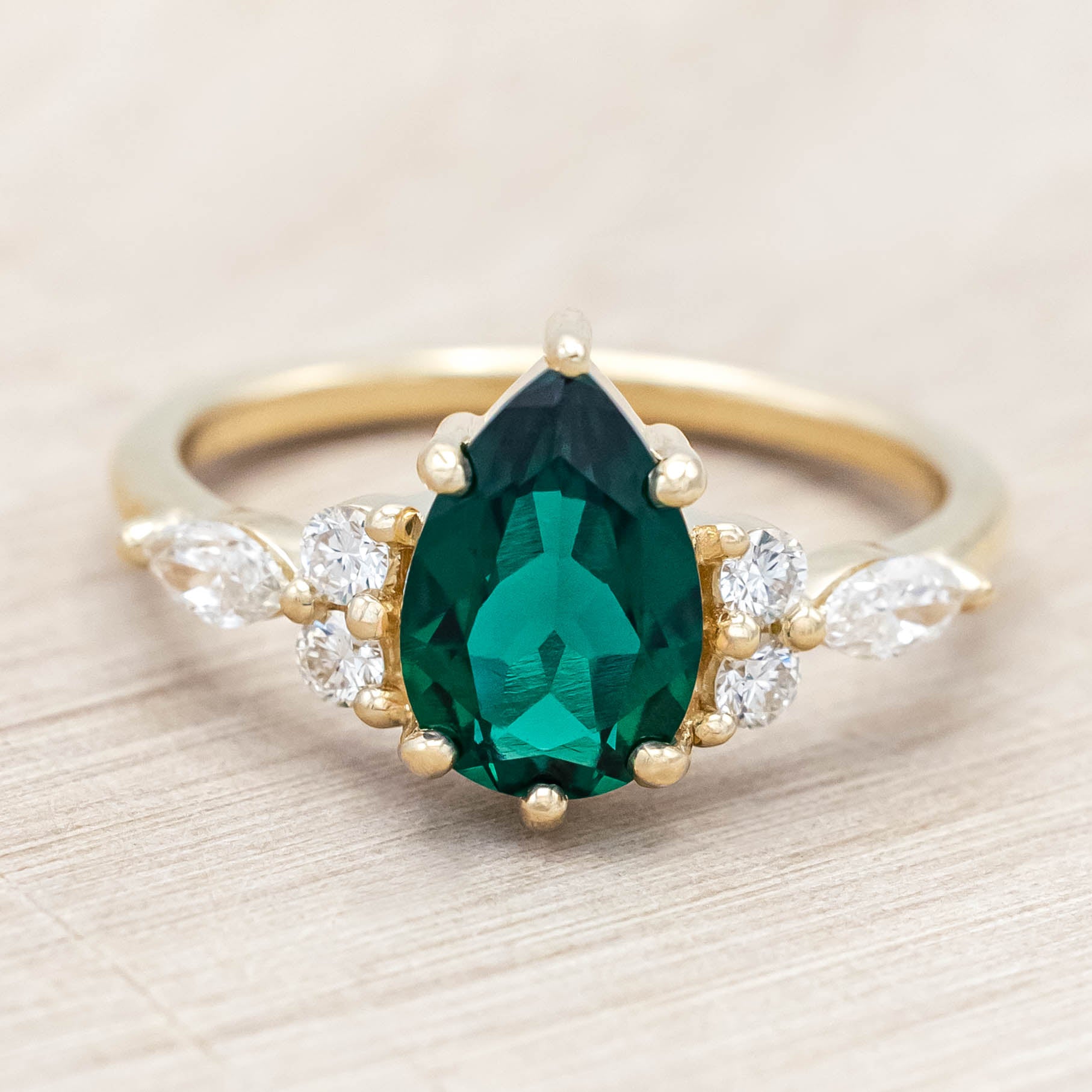 Gold ring with a green emerald and smaller diamond accents on a light wooden surface