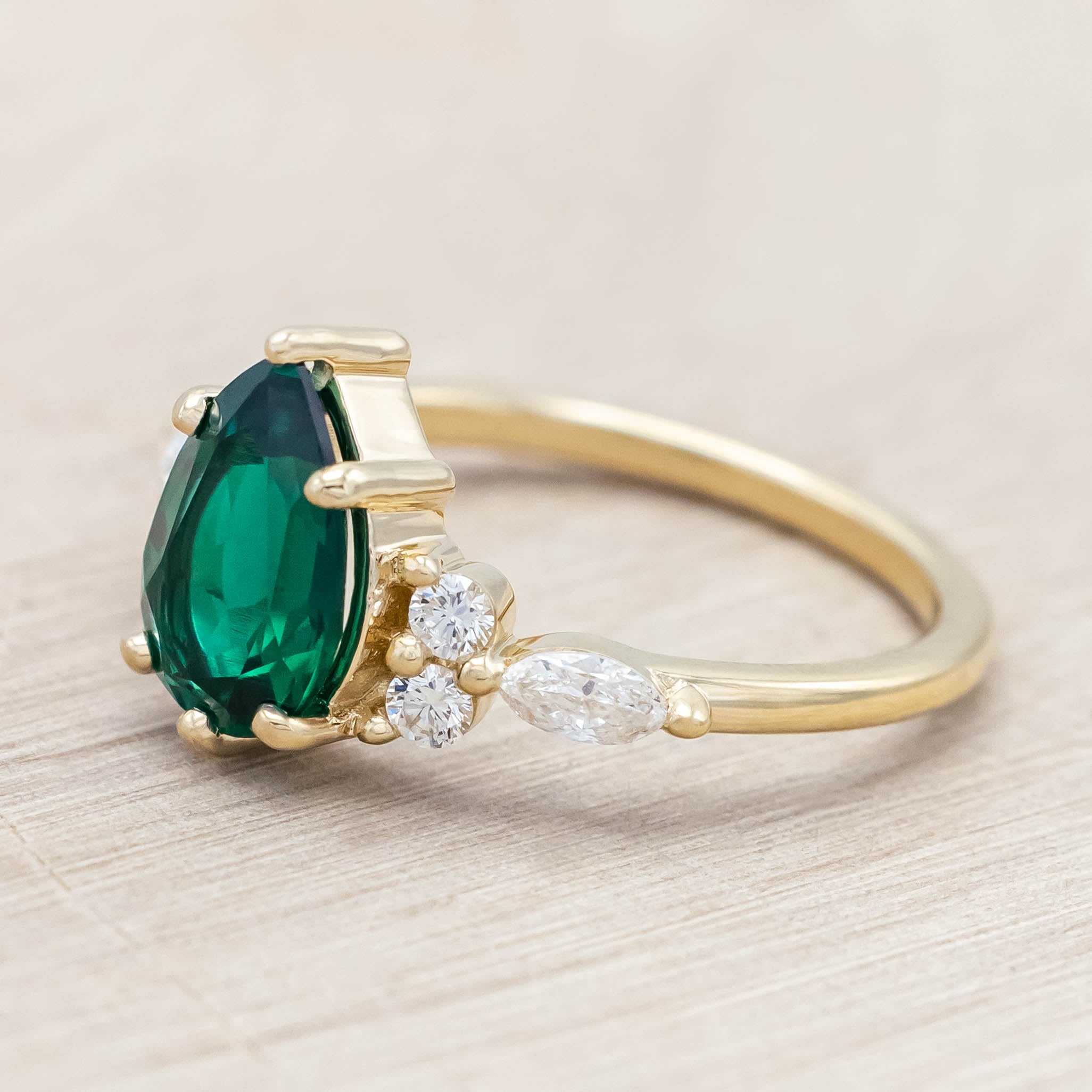 Gold ring with a green emerald and smaller diamond accents on a light wooden surface