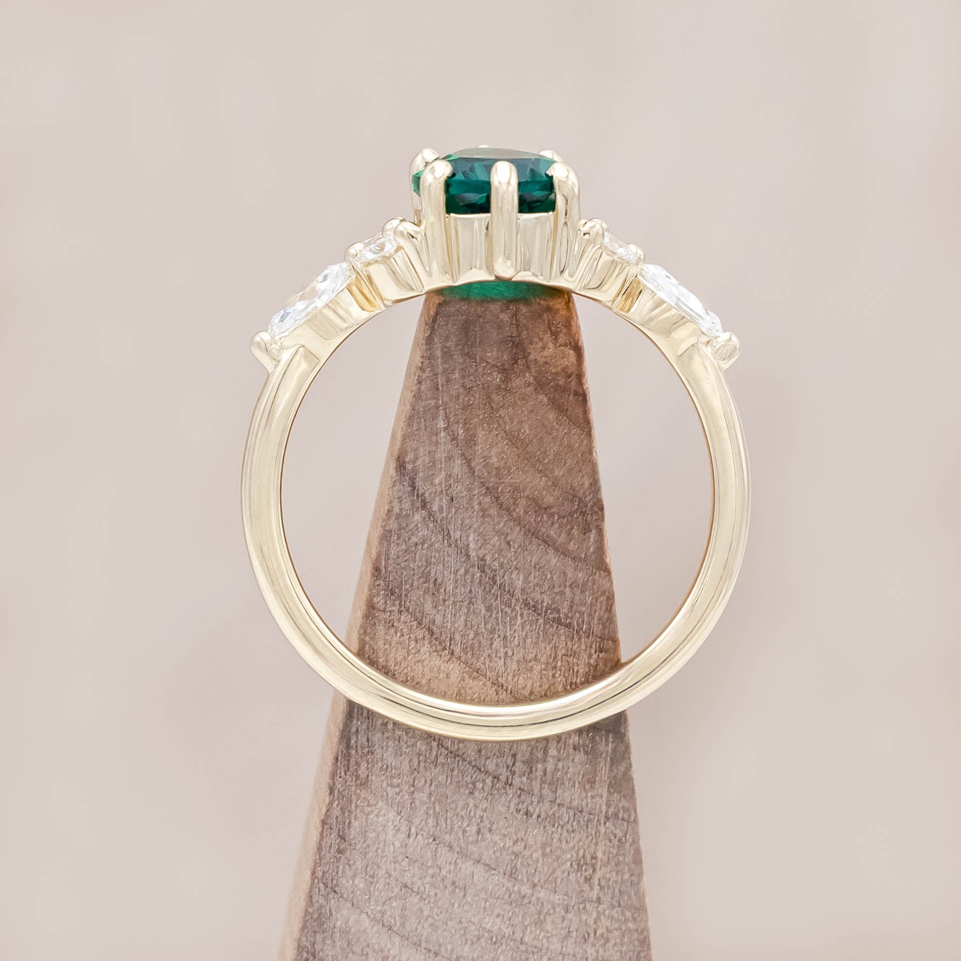 Gold ring with a green emerald and smaller diamond accents on a light wooden surface