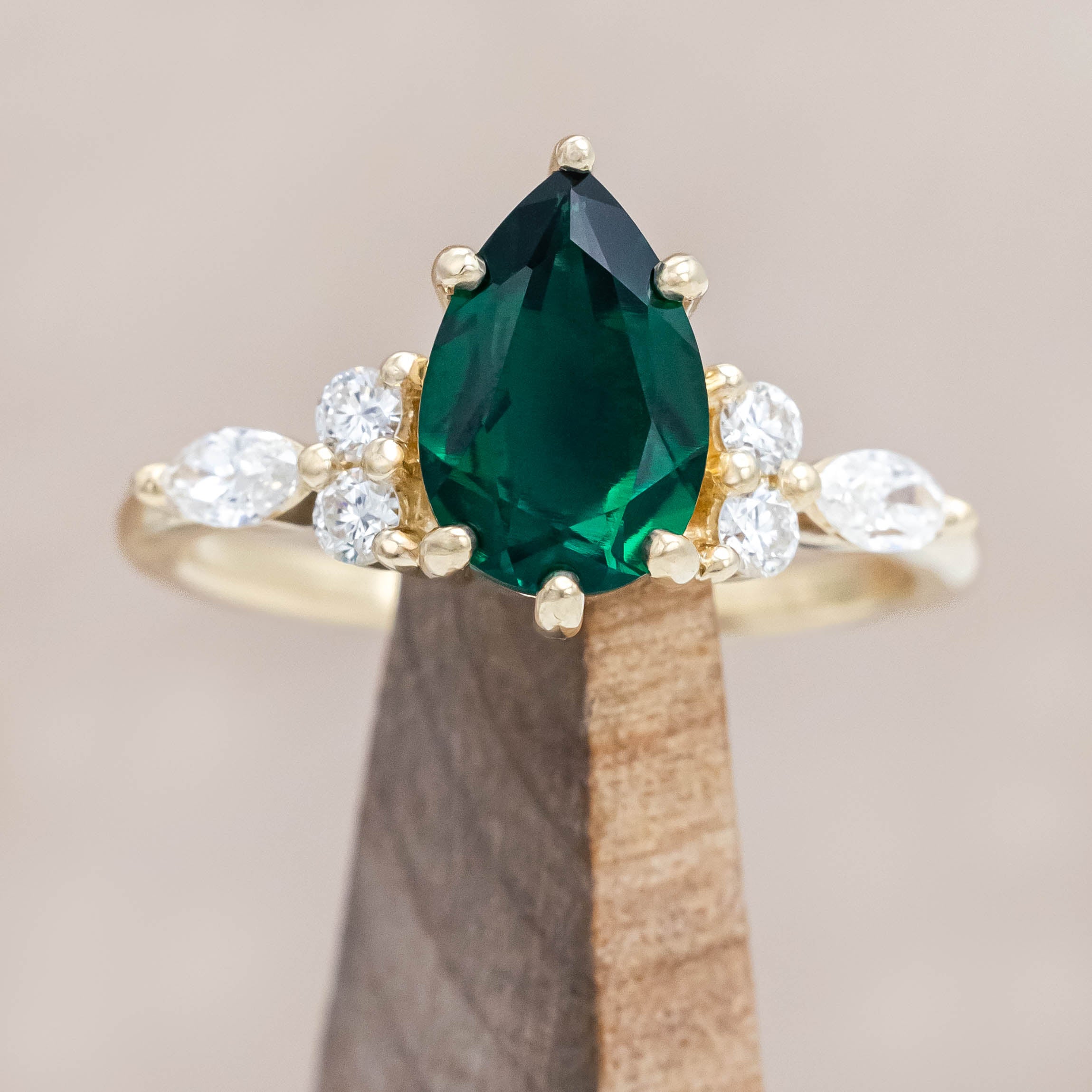 Gold ring with a green emerald and smaller diamond accents on a neutral background