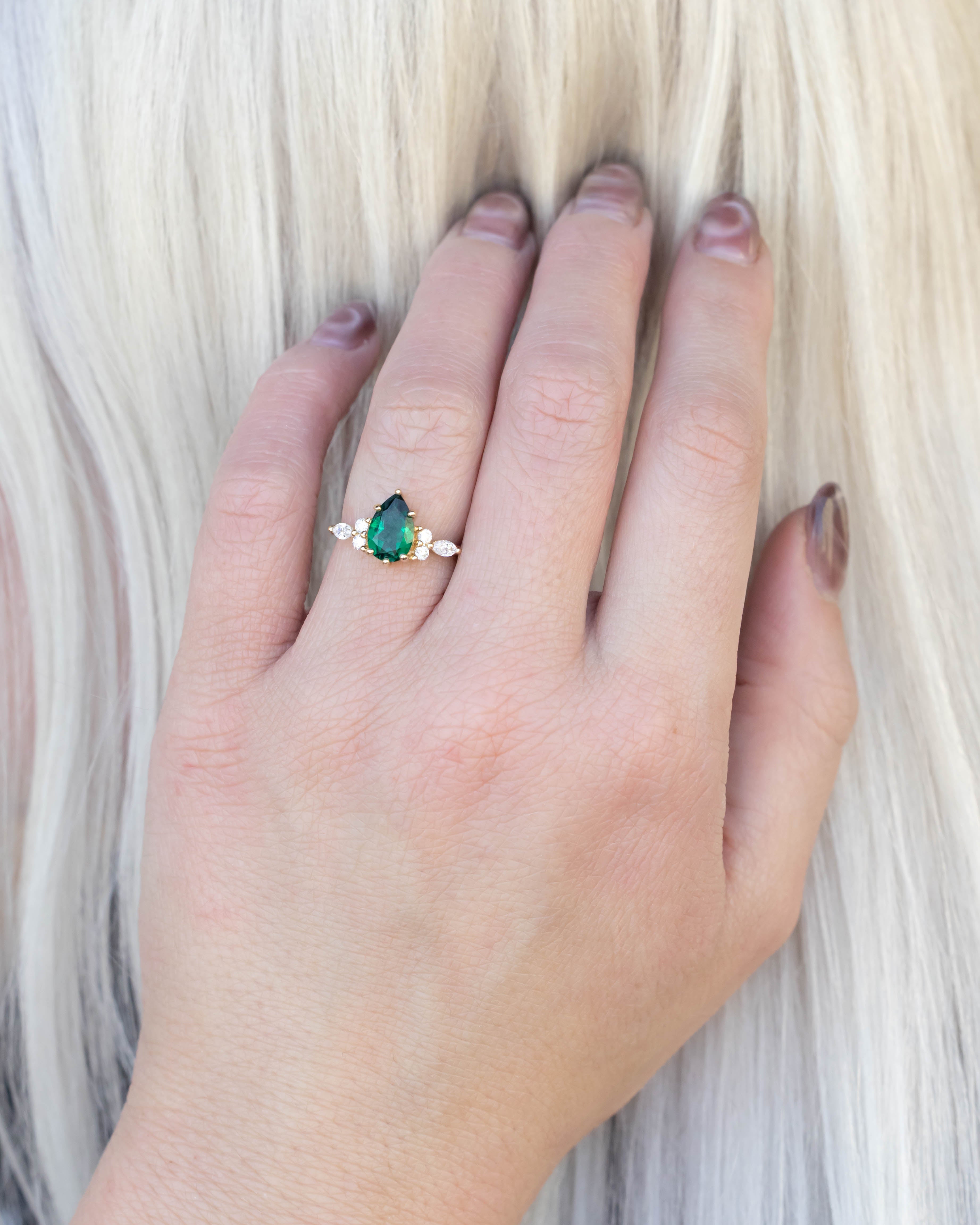 Hand wearing a ring with a green emerald against a neutral background