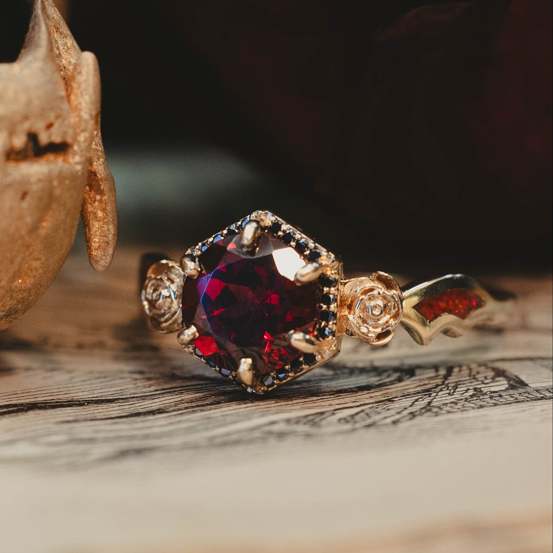Gold ring with a red gemstone on a wooden surface with a skull in the background
