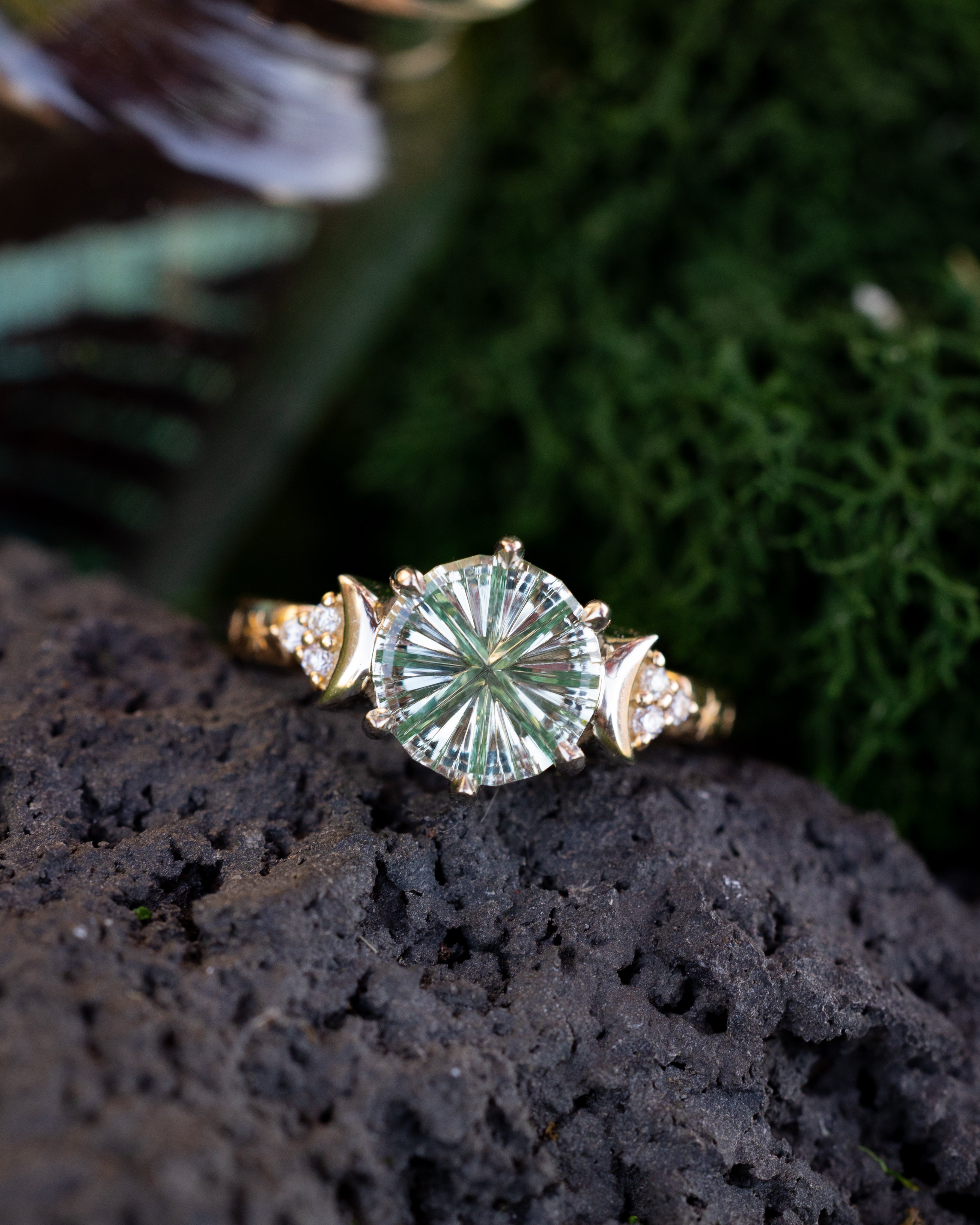 Gold ring with a green sapphire on a dark surface with green foliage in the background