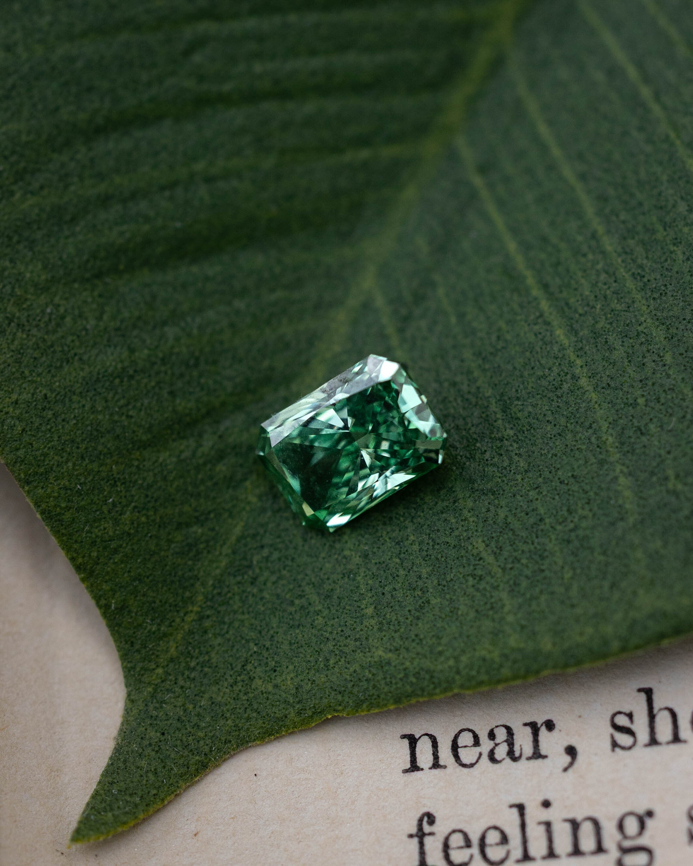 Green lab diamond sitting on top of a green leaf and piece of paper