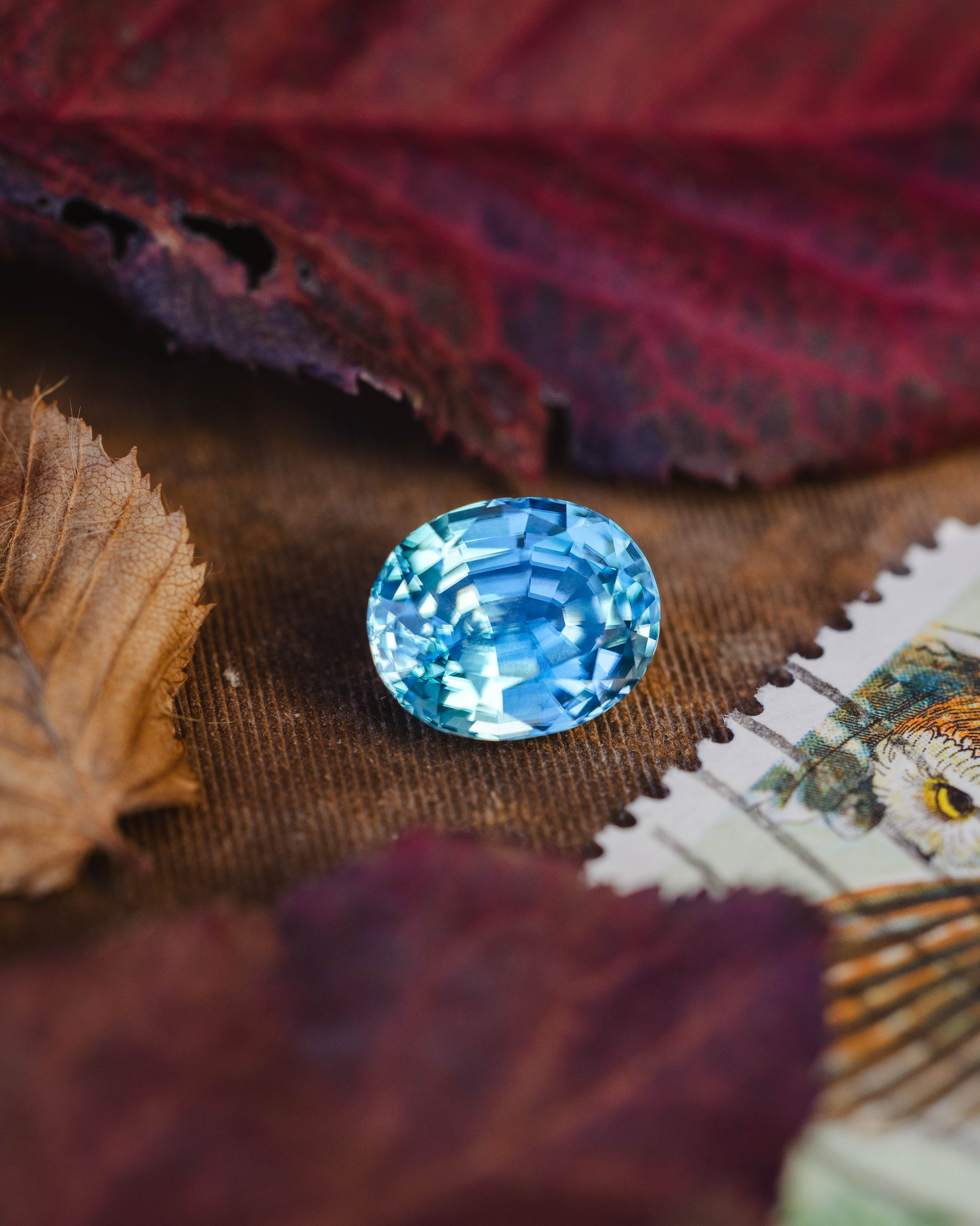 Blue zircon on a textured surface with leaves and fabric