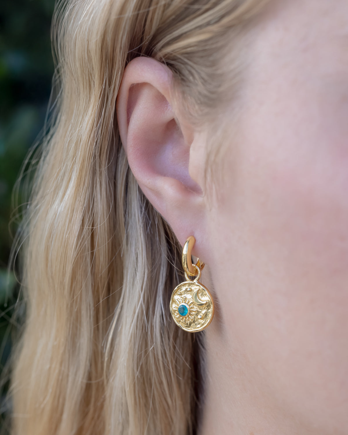 Person with blond hair wearing gold dangle earring with a moon and sun design and apatite accent