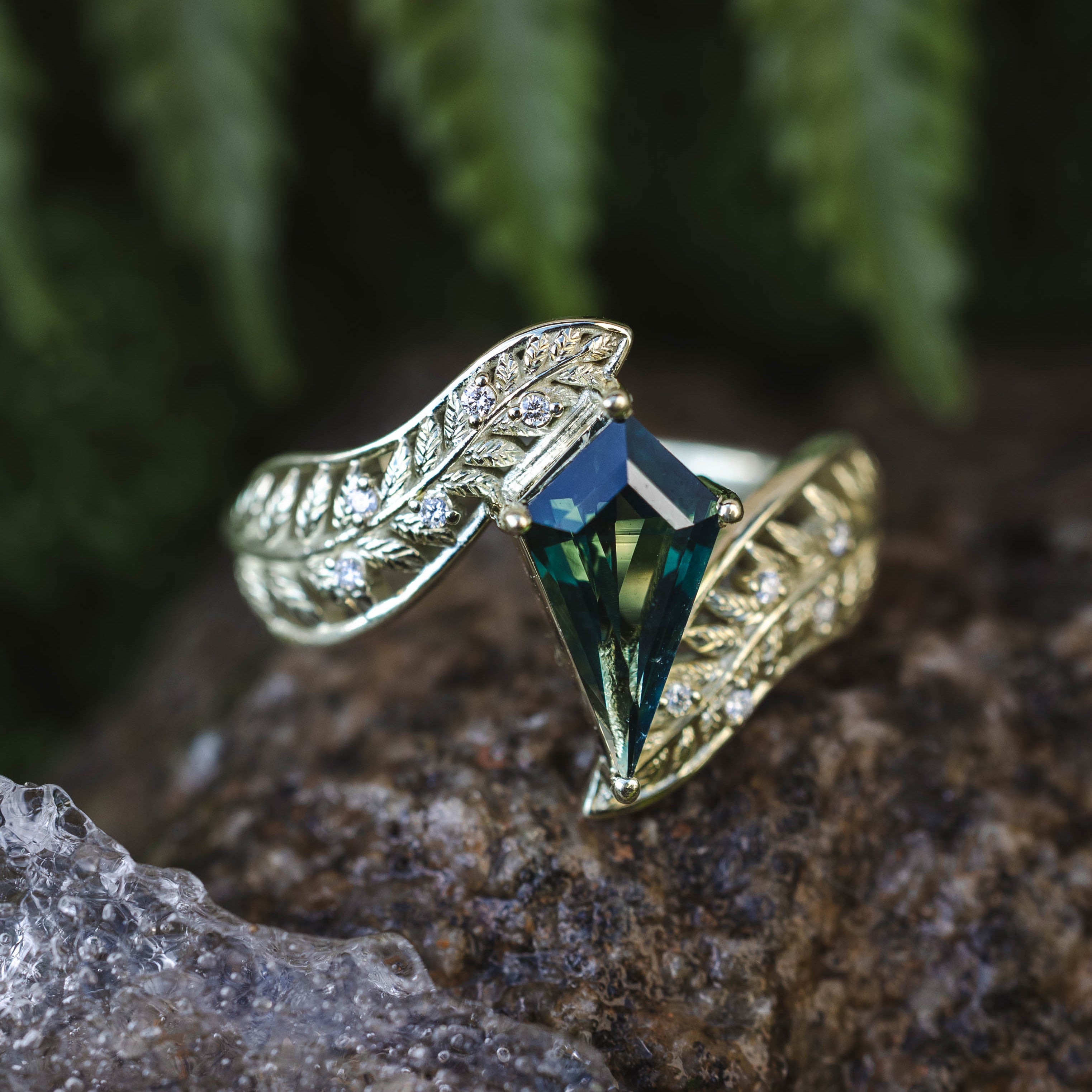 Green gold ring with a green sapphire gemstone on a rock with ferns in the background
