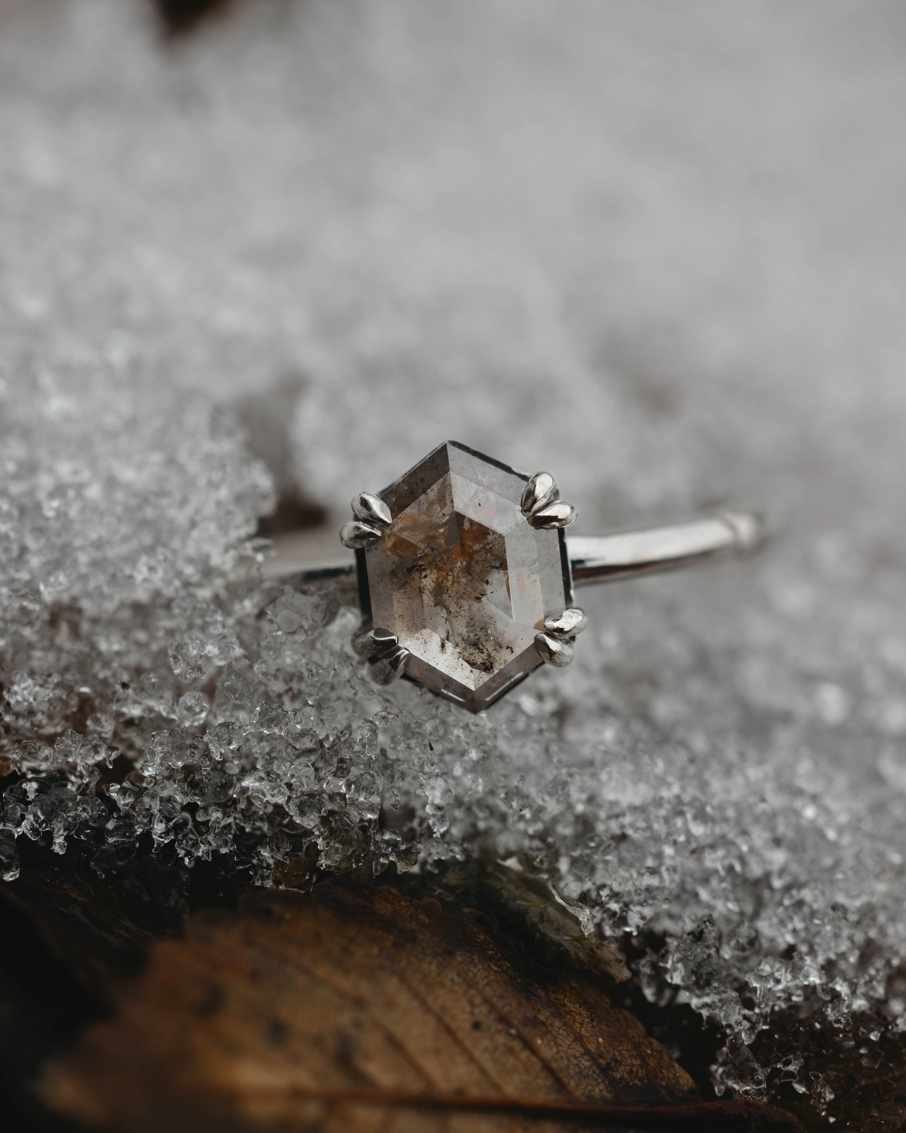 White gold ring with a hexagonal salt & pepper diamond on a snowy surface