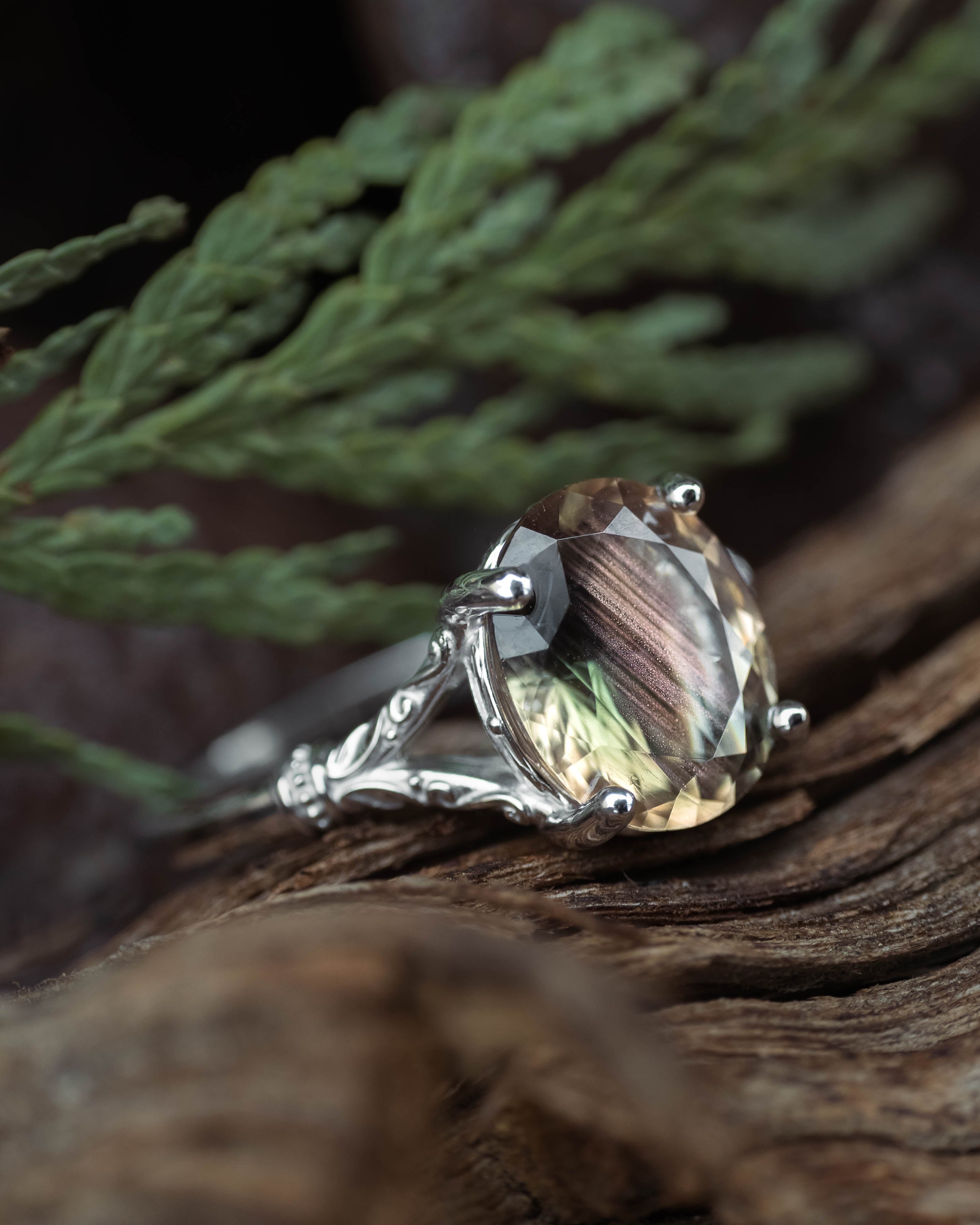 White gold ring with a oval sunstone on a wooden surface with greenery in the background