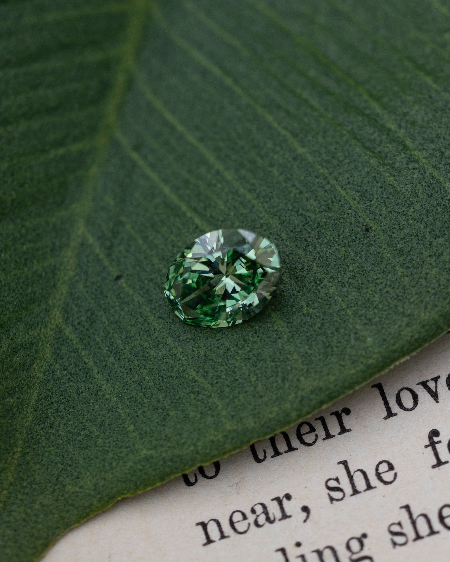 Green lab diamond sitting on top of a green leaf and piece of paper
