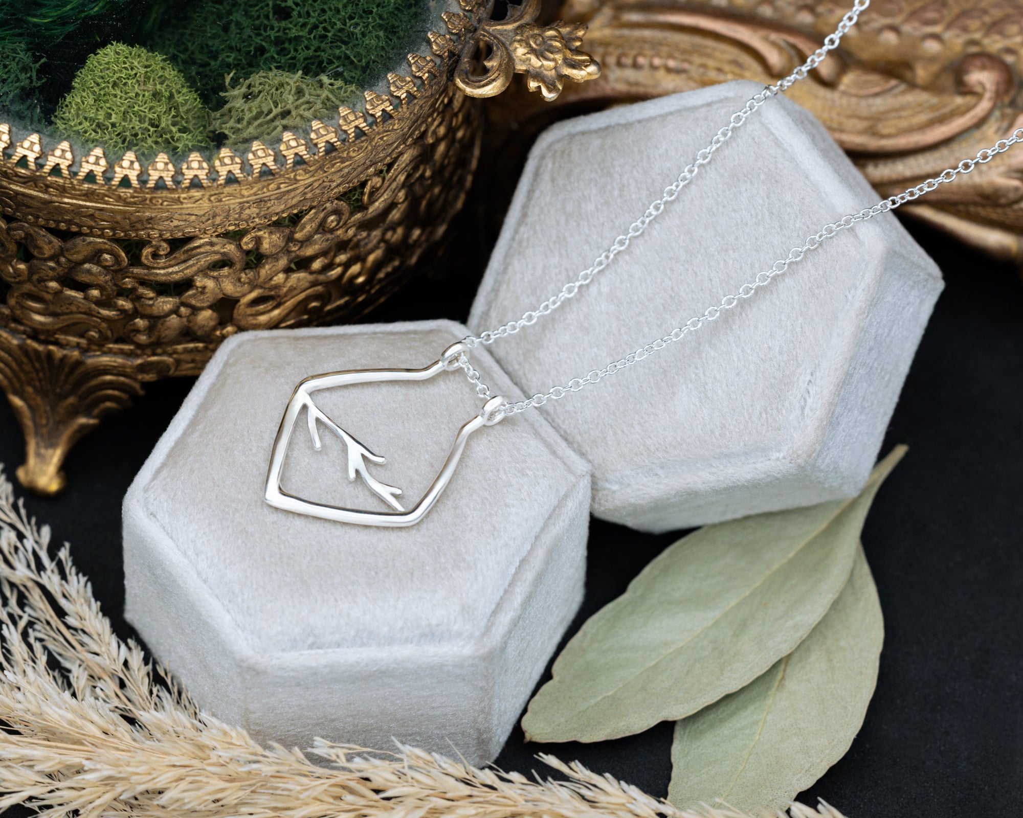 A silver necklace with antler design on a white cushion with blurred dried flowers