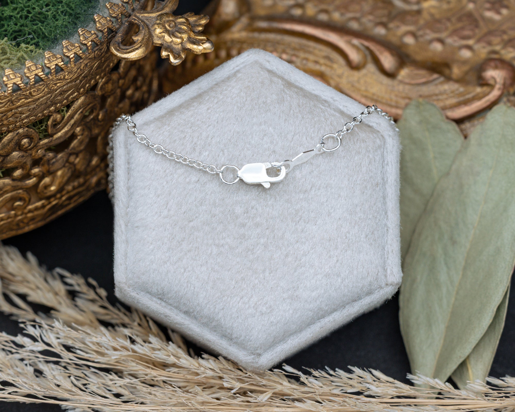 Back of silver chain with clasp on a white cushion against a dried floral backroud