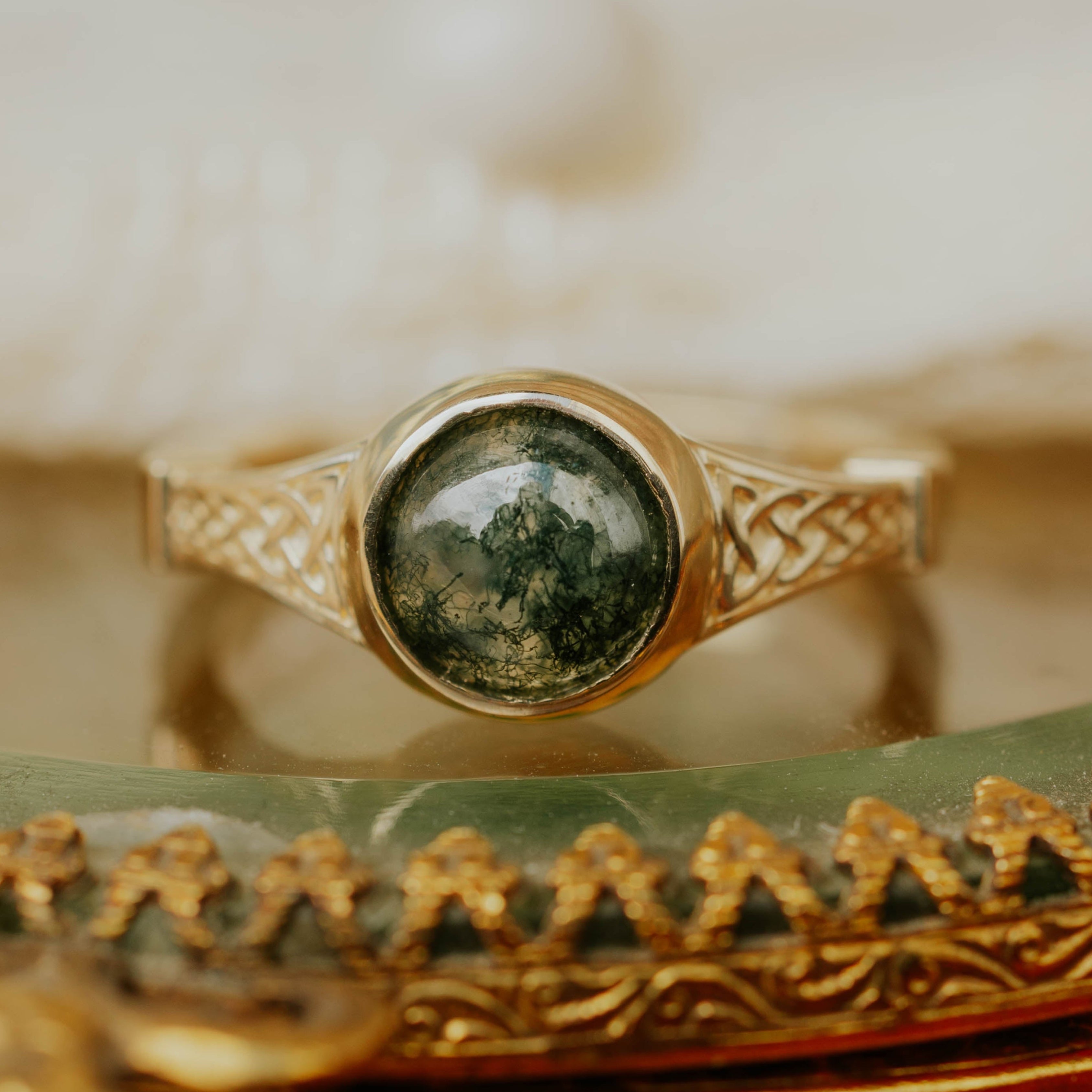 Gold engagement ring with moss agate on an ornate gold stand.