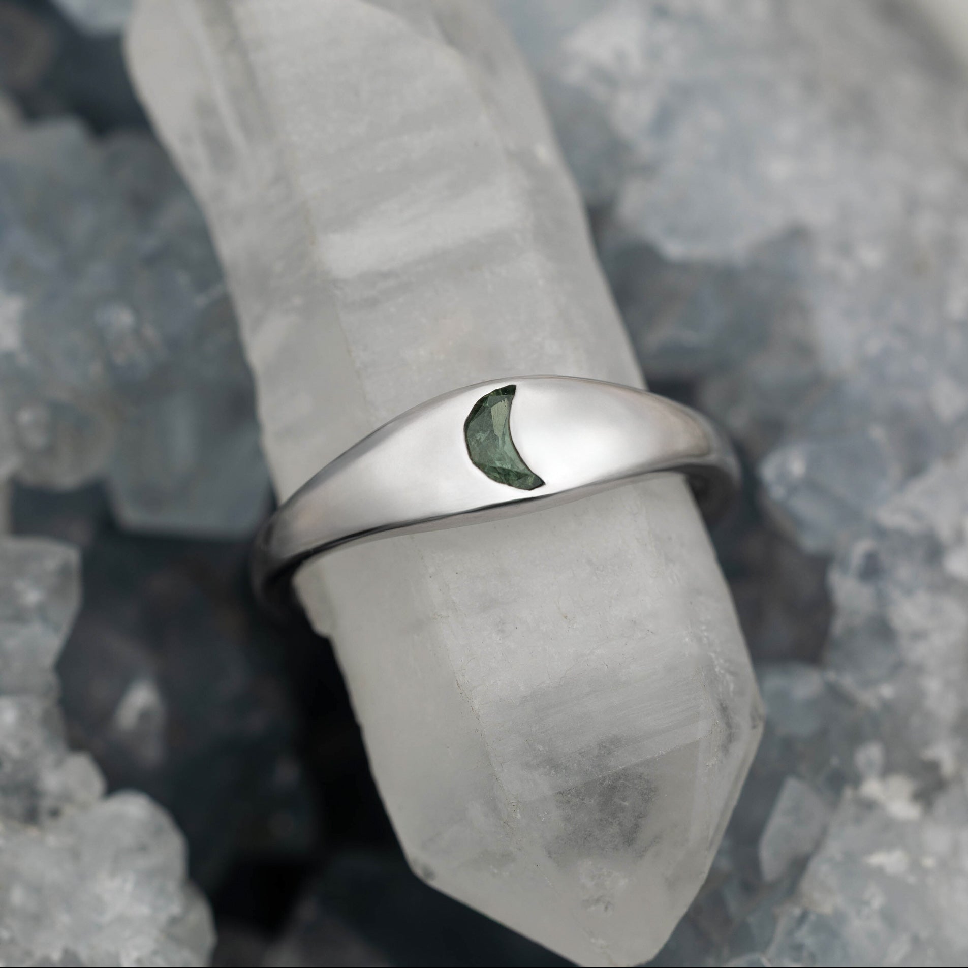 White gold ring with a green sapphire on a gray stone surface