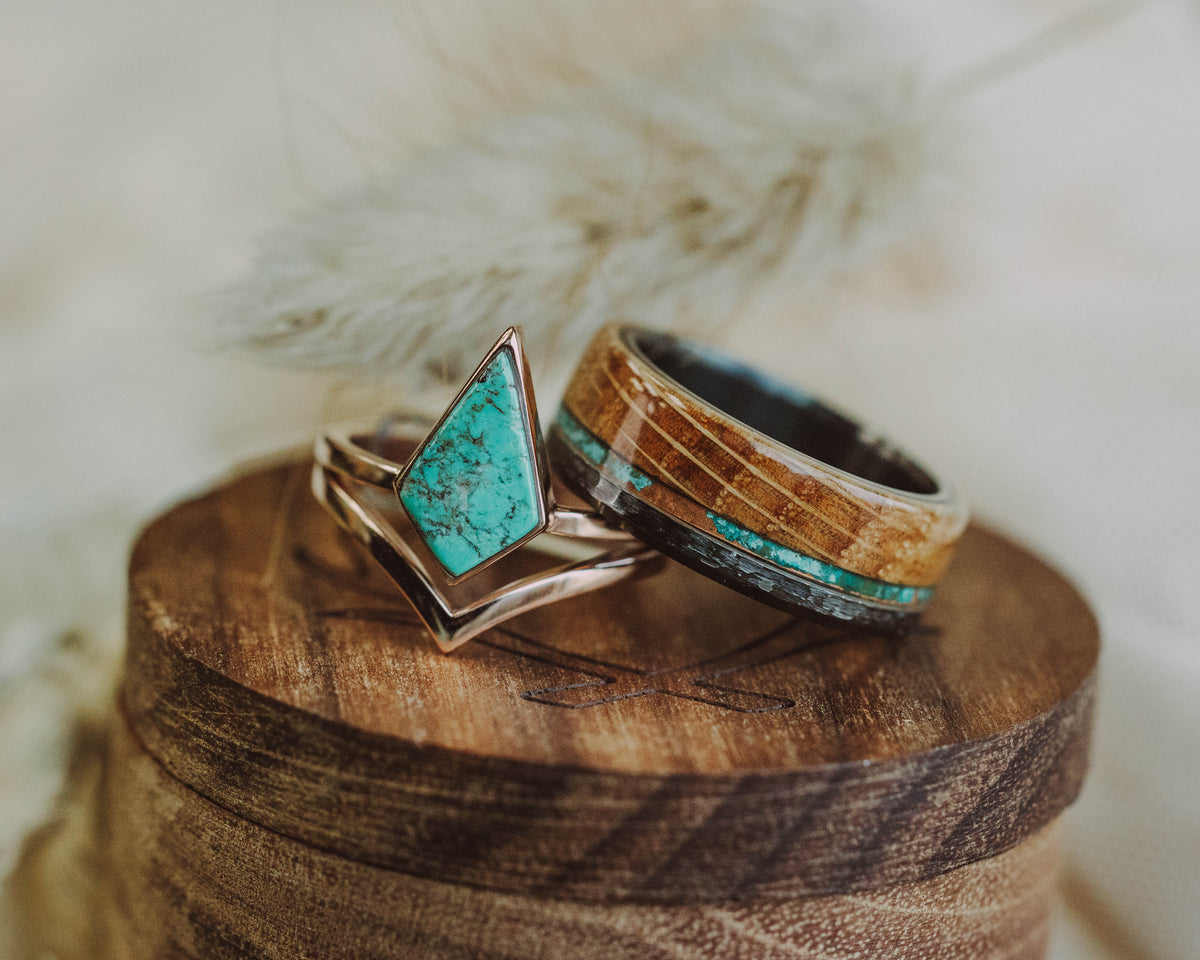 Turquoise engagement ring next to a whiskey barrel wedding band on a wooden ring box