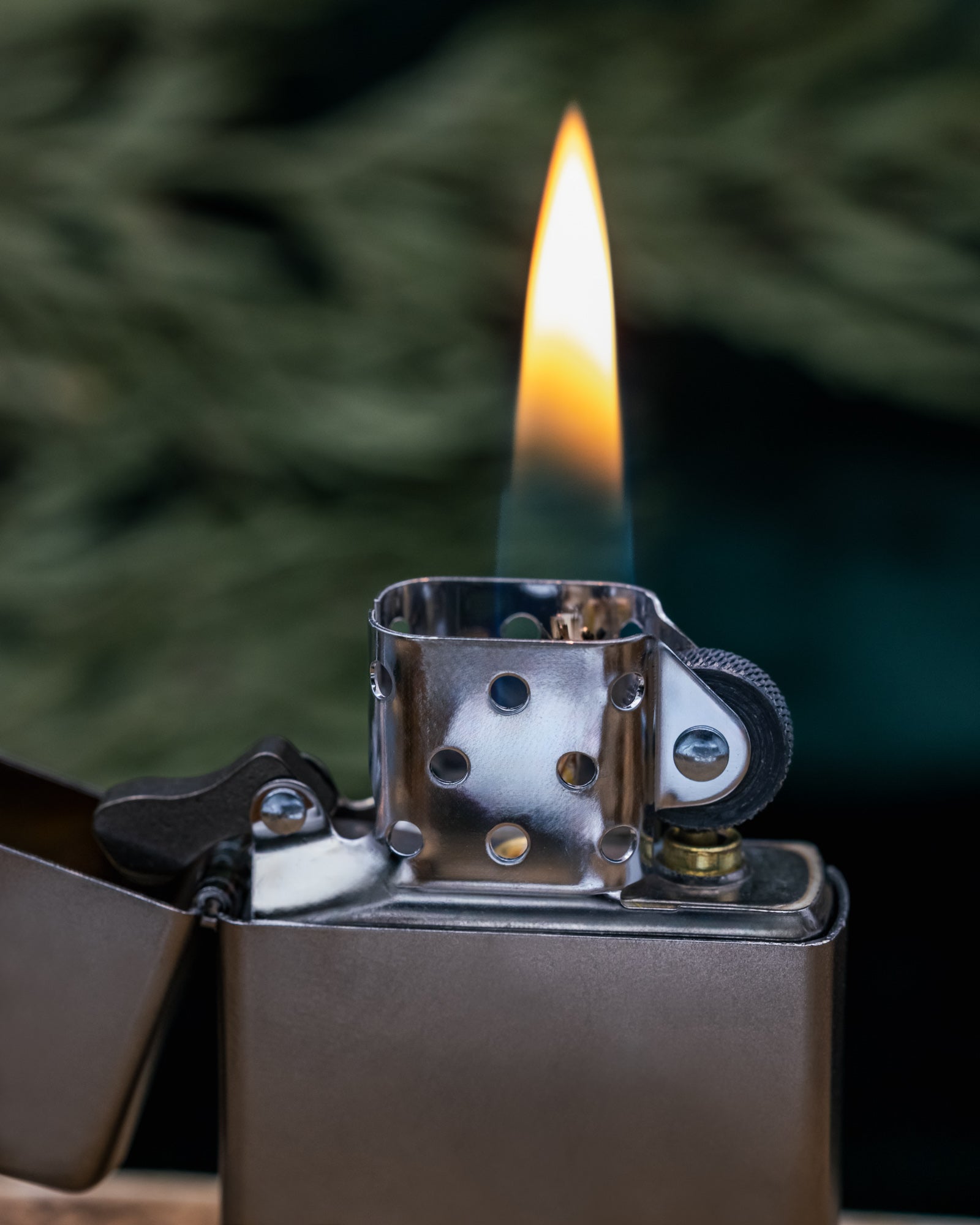 Zippo lighter with a lit flame against a blurred green background