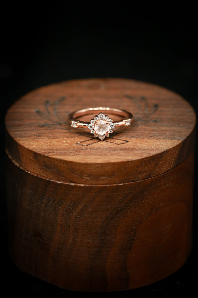 Shown here is  The "Starla", a halo-style round rose quartz women's engagement ring with delicate and ornate details and is available with many center stone options
