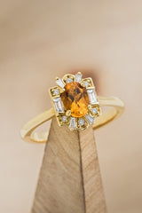 Shown here is"Cleopatra", a women's birthstone ring with a citrine center stone and diamond halo, on stand facing slightly right. Many other center stone options are available upon request.