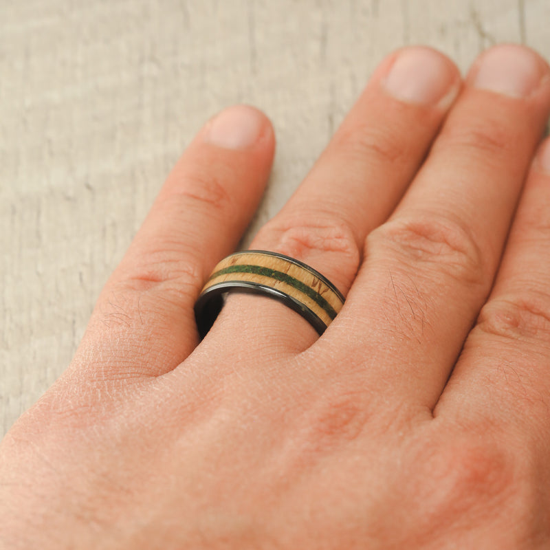 Shown here, Rainier, is a handcrafted men's wedding ring featuring moss and spalted maple wood inlays on a fire-treated black zirconium band on hand. Additional inlay options are available upon request.