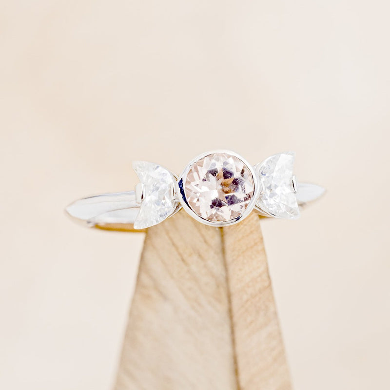 Shown here is "Candi", a bezel set, knife-edged women's engagement ring with a round morganite and two crescent moon moissanite accents