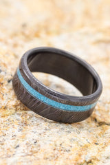 Shown here is : "Vertigo",a custom, handcrafted men's wedding ring featuring a turquoise inlay, shown here on a fire-treated black zirconium band with a woodgrain finish. Additional inlay options are available upon request.