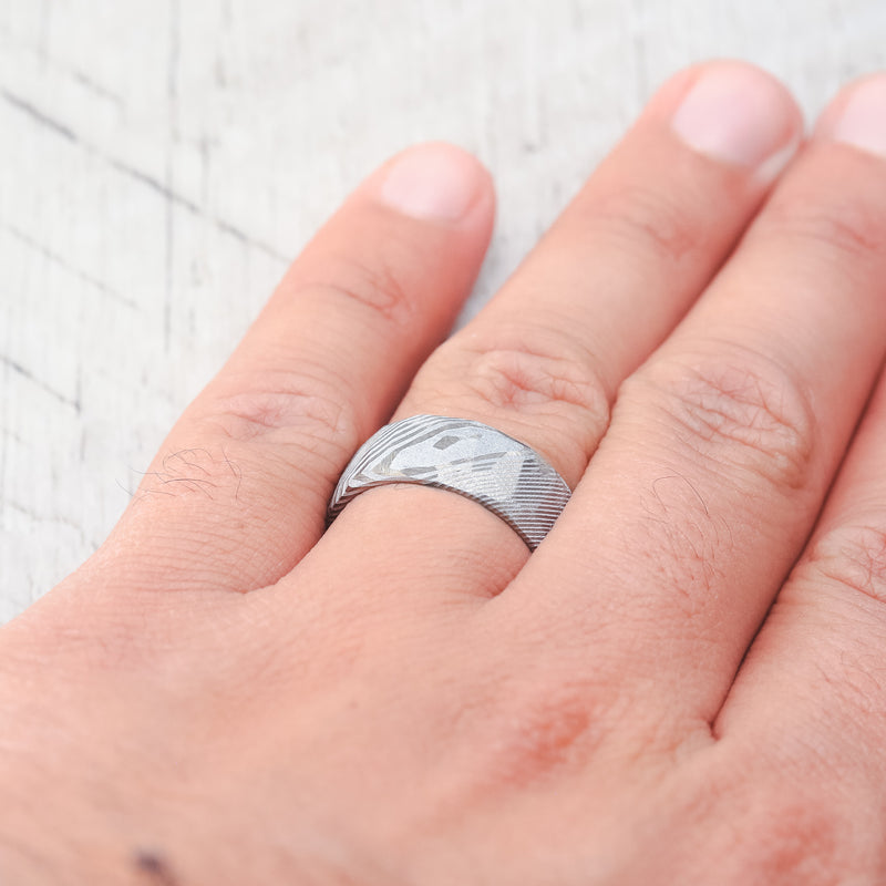 Shown here, a handcrafted men's wedding ring featuring a faceted Damascus steel wedding band with an etched finish. Additional inlay options are available upon request.