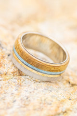 Shown here is  "Banner", a custom, handcrafted men's wedding ring featuring a thin 14k yellow gold inlay, set next to turquoise, whiskey barrel wood, and naturally shed antler, shown here on a titanium band. Additional inlay options are available upon request.