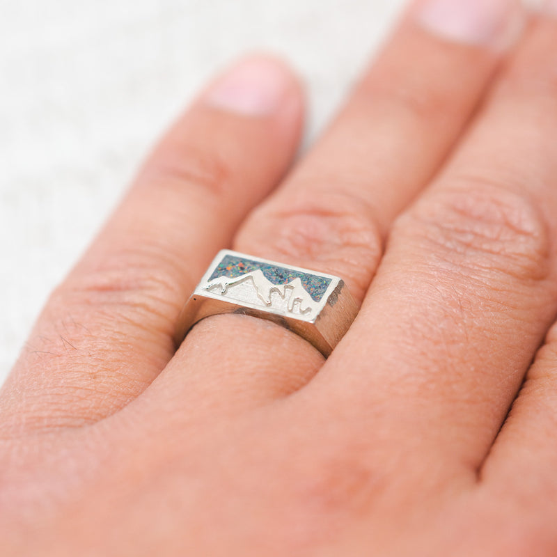 Shown here, Atlas,  a custom, handcrafted men's wedding ring featuring a crushed fire and ice opal inlay and a mountain range engraved into a 14K gold band, on hand.  Additional inlay options are available upon request.