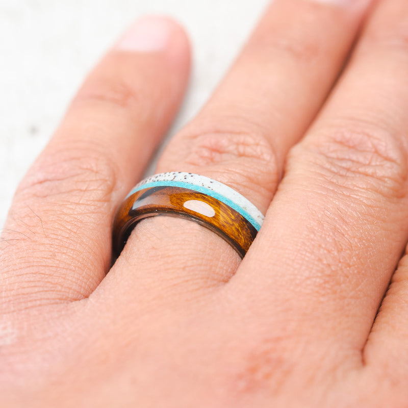 Shown here, Banner, a custom, handcrafted men's wedding ring featuring ironwood and naturally shed antler with a turquoise inlay on a titanium band, on hand. Additional inlay options are available upon request.