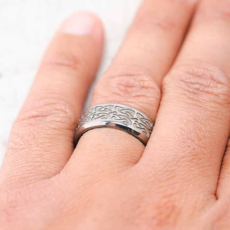 Shown here, a handcrafted men's wedding ring featuring a solid band with Celtic love knot engravings, on hand.