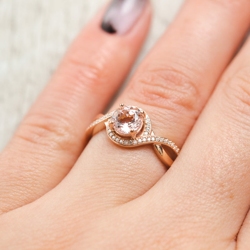 Shown here, Charlotte a round cut morganite twisted women's engagement ring with a diamond halo and diamond accents, on hand,  Many center stone options are available upon request. 