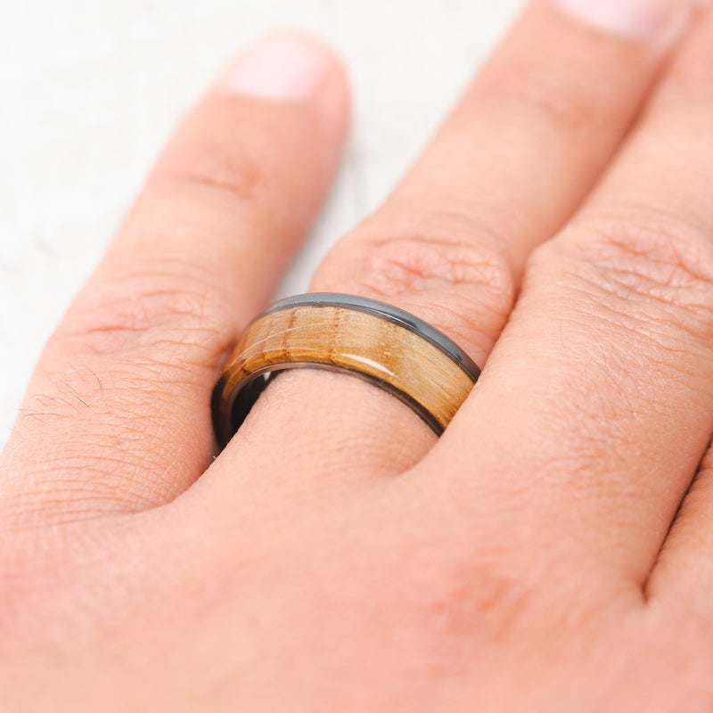 Shown here, Ezra, a custom, handcrafted men's wedding ring featuring a whiskey barrel oak overlay, on hand. Additional inlay options are available upon request.