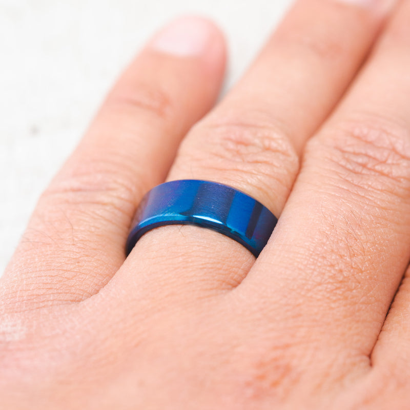 Shown here, a handcrafted men's wedding ring featuring a fire-treated titanium band, on hand. 