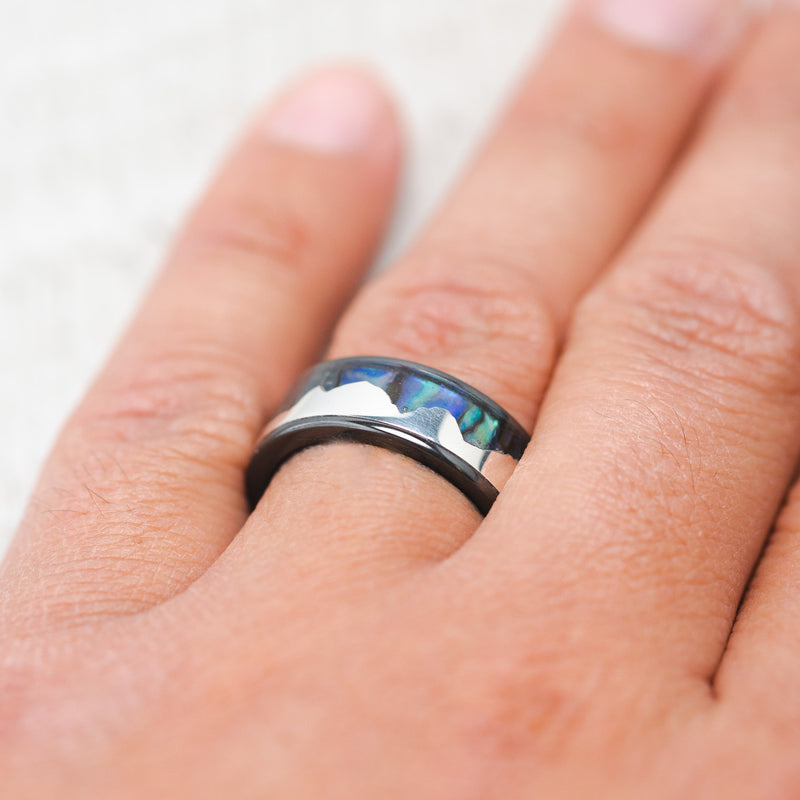 Shown here is, "Helios", a custom, handcrafted men's wedding ring featuring a mountain range using pieces of silver and paua shell inlay, on hand. Additional inlay options are available upon request.
