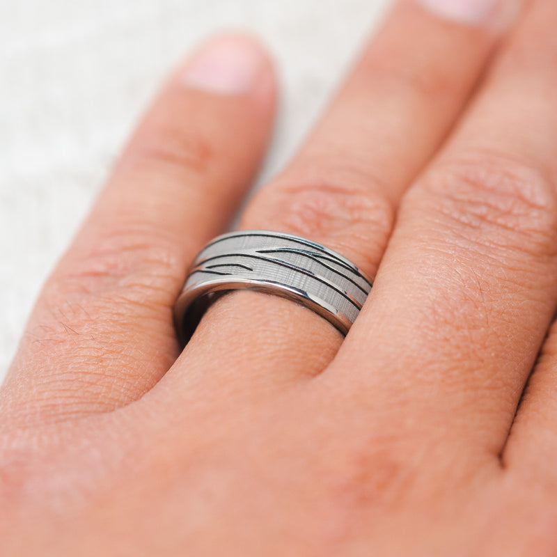 Shown here, Legacy, a handcrafted, embossed men's wedding ring featuring a branch engraving in a channel-style band, on hand. It can be customized to feature just about any embossed design you can dream up.