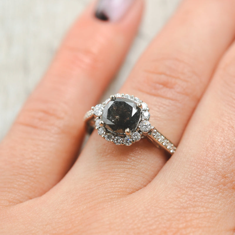 Shown here, Ophelia, a women's engagement ring with a diamond halo and diamond accents displayed here with a cushion cut salt and pepper diamond but listed here as a mounting-only option, on hand. Follow the instructions above to select your stone.