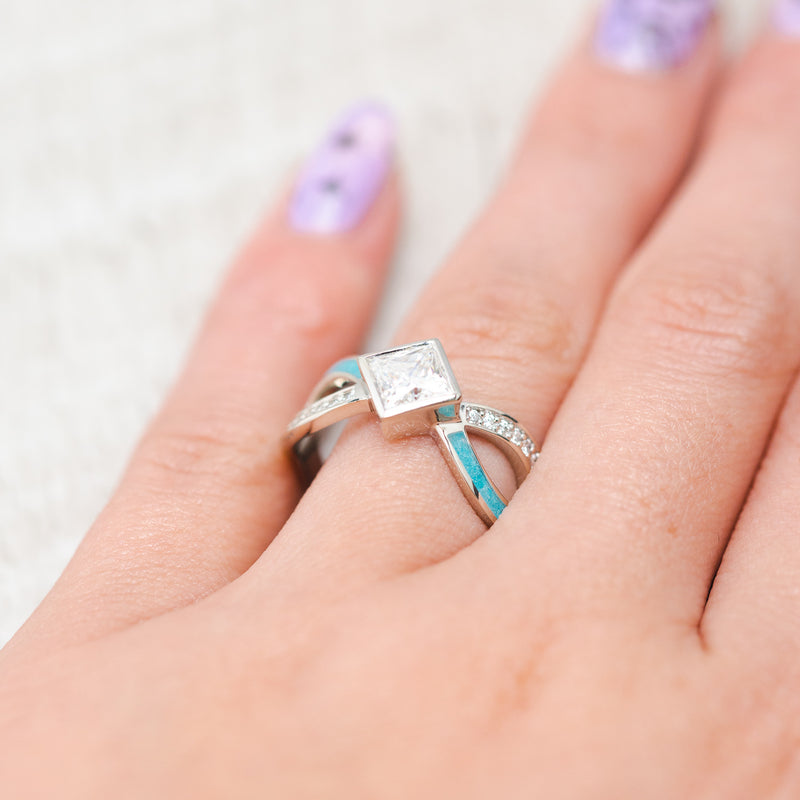 Shown here, a bezel set moissanite women's engagement ring with diamond accents and turquoise inlays, on hand. Many other center stone options are available upon request. 