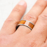 Shown here, Rainier, a custom, handcrafted men's wedding ring featuring a koa wood inlay, on hand. Additional inlay options are available upon request.