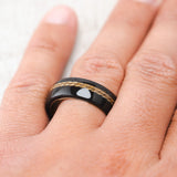 Shown here, Remmy,  a custom, handcrafted men's wedding ring featuring an African black wood overlay and gold nugget inlay, shown here on a titanium band, on hand. Additional inlay options are available upon request.
