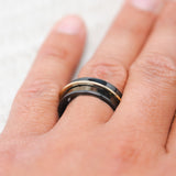 Shown here, Rotary,  a handcrafted concave men's wedding ring featuring a free-spinning 14K yellow gold band, on hand. Shown here set on a black zirconium wedding band. Additional inlay options are available upon request.