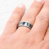 Shown here, Sedona, a handcrafted men's wedding ring featuring a solid black zirconium band with hammered edges, on hand. The band was fire-treated before the edges were hammered causing the edges to be grey.